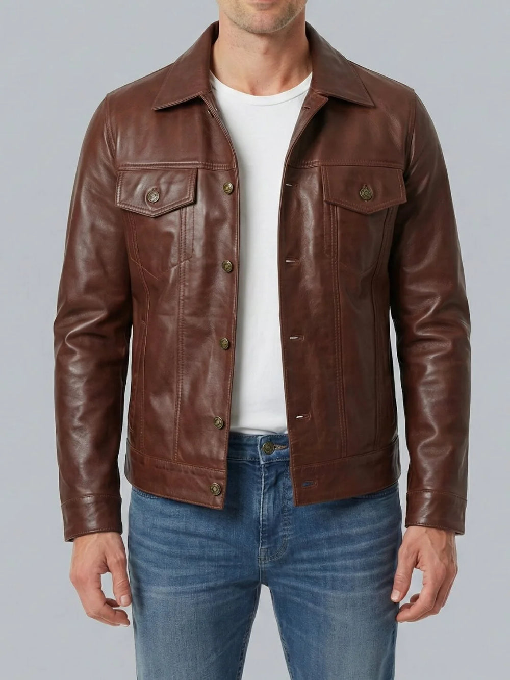 Man wearing a brown leather jacket over a white shirt and blue jeans on a gray background
